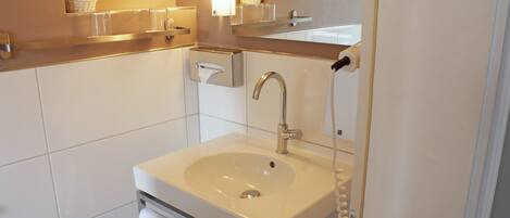 Un baño moderno con un lavabo blanco, un espejo y un perchero para toallas.