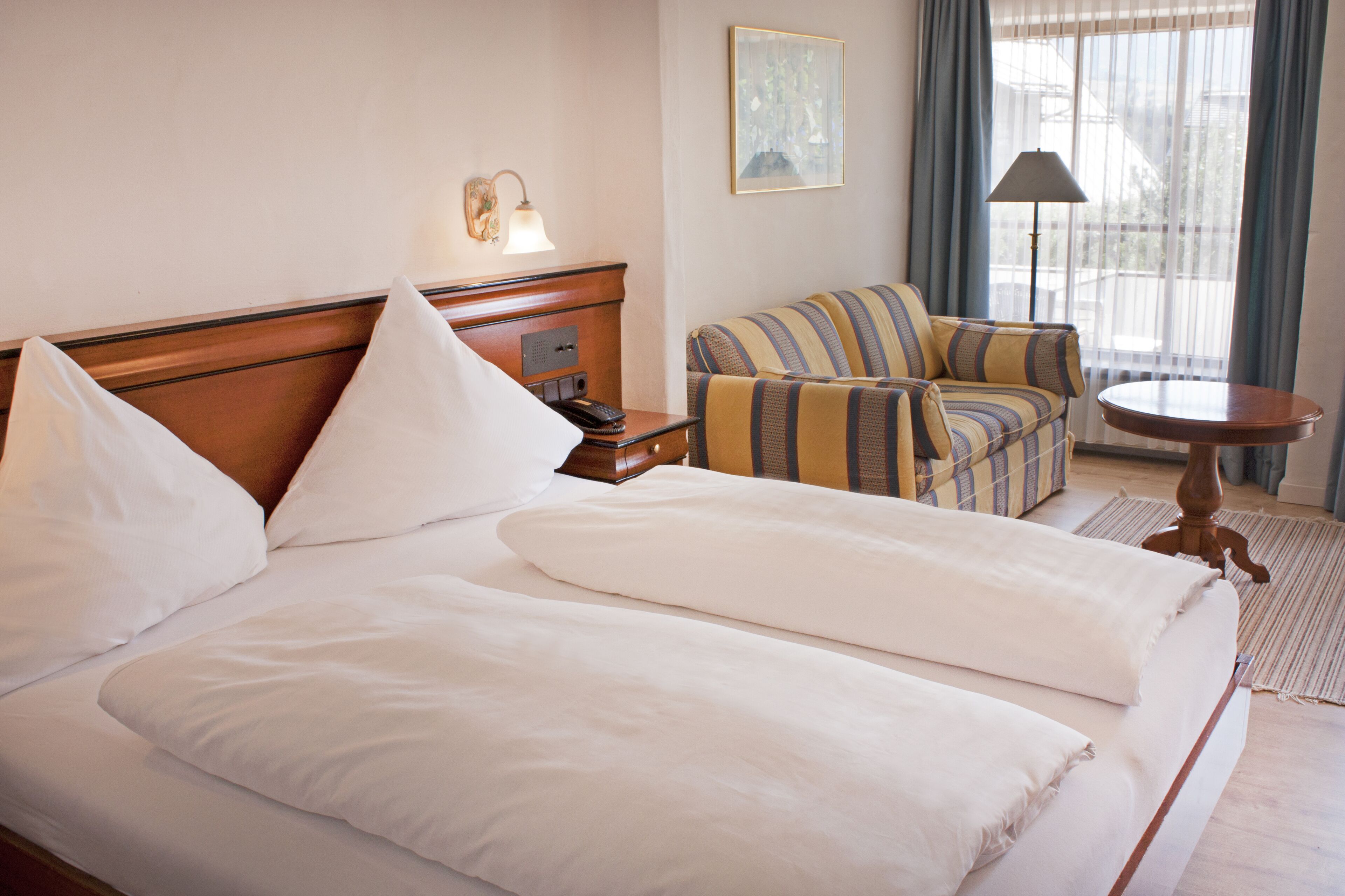Una habitación de hotel con una cama grande, una mesita de noche, una lámpara, un sofá y una pequeña mesa.
