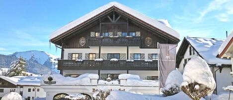 A large, multi-story building with a snow-covered roof and balcony, surrounded by snow.