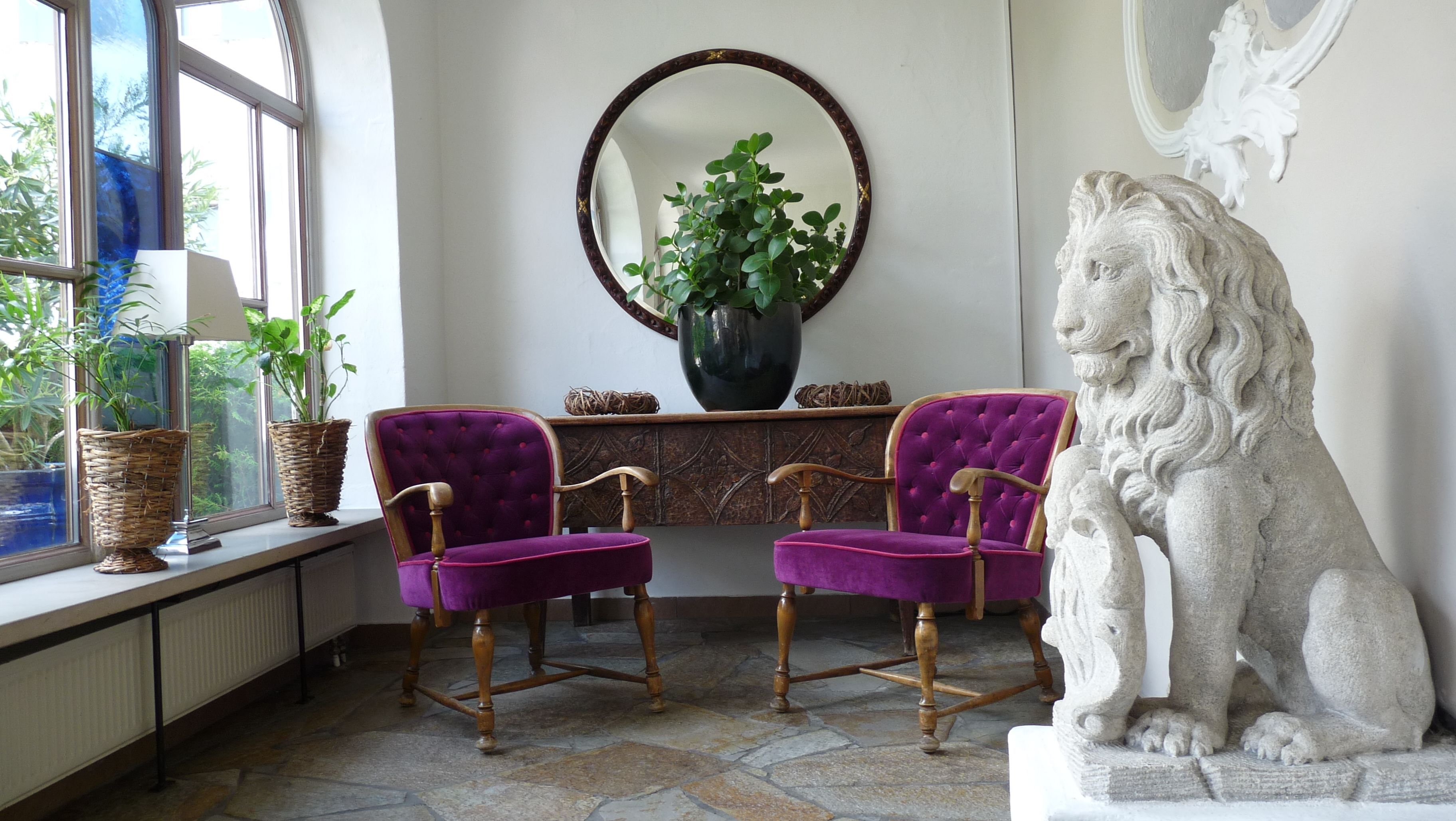 A room with two purple velvet chairs, a stone lion statue, a large mirror, and a potted plant.