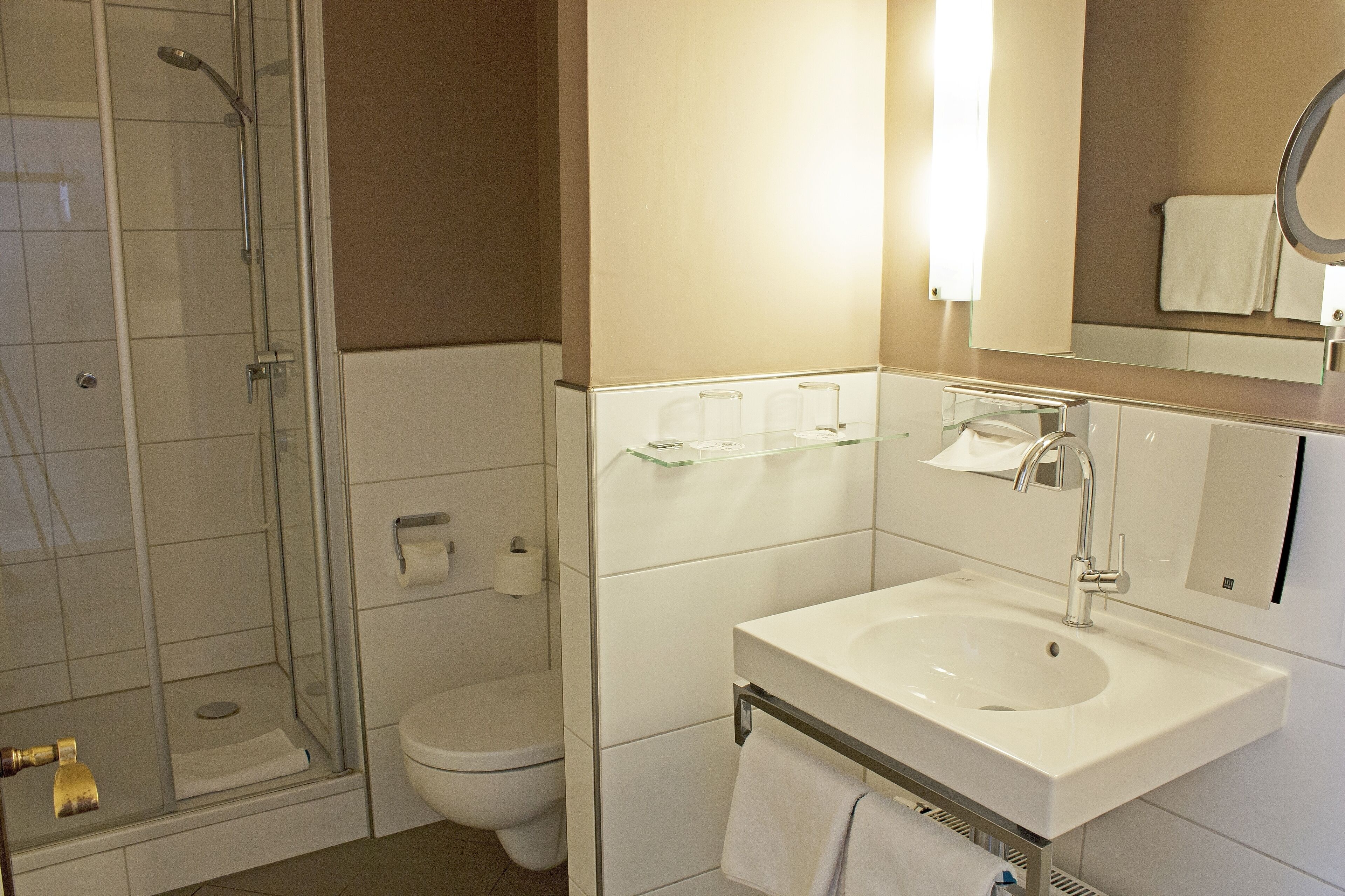 Un baño moderno con cabina de ducha de vidrio, lavabo blanco con espejo y retrete.