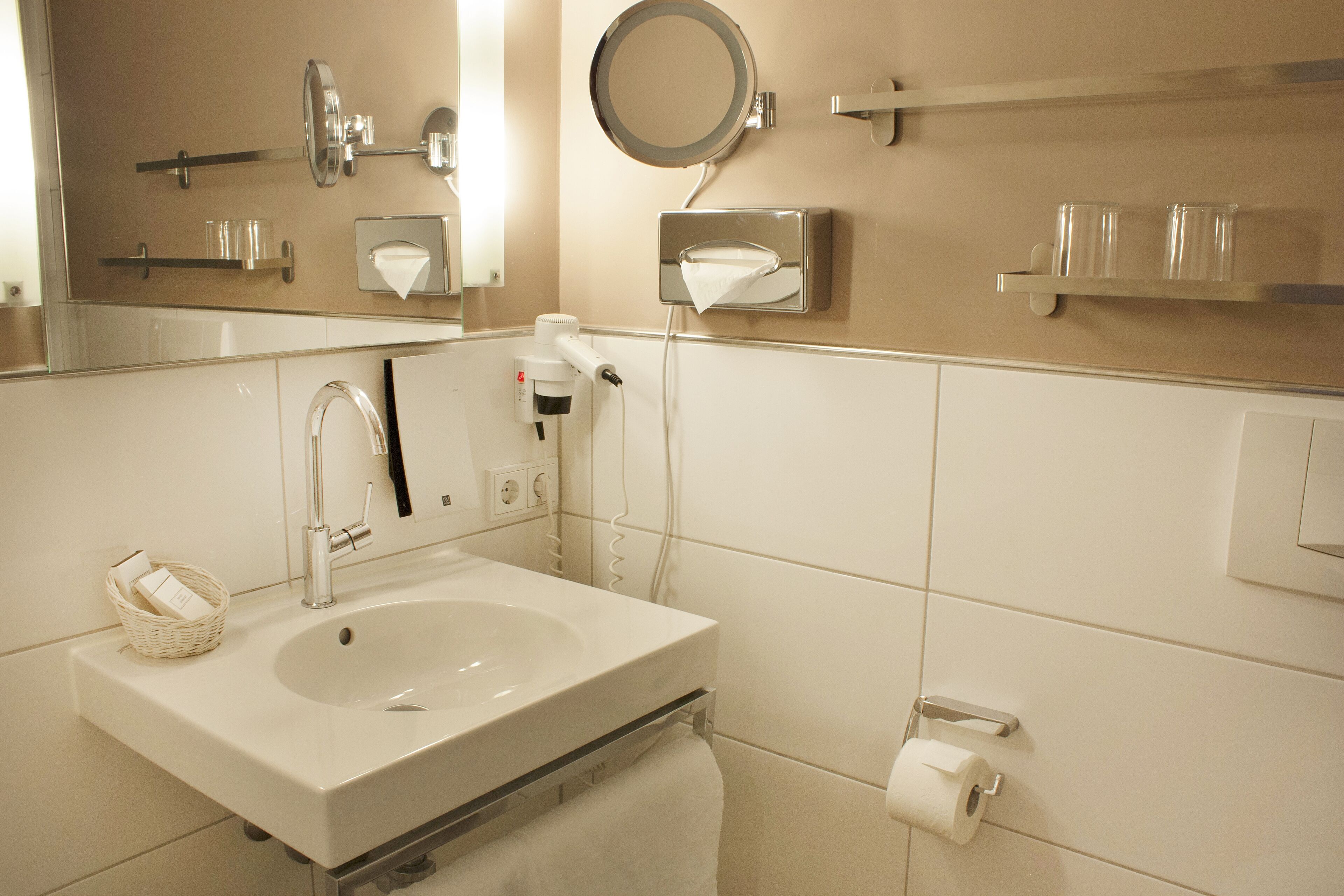 A bathroom with a sink, mirror, towel dispenser, and toilet paper.