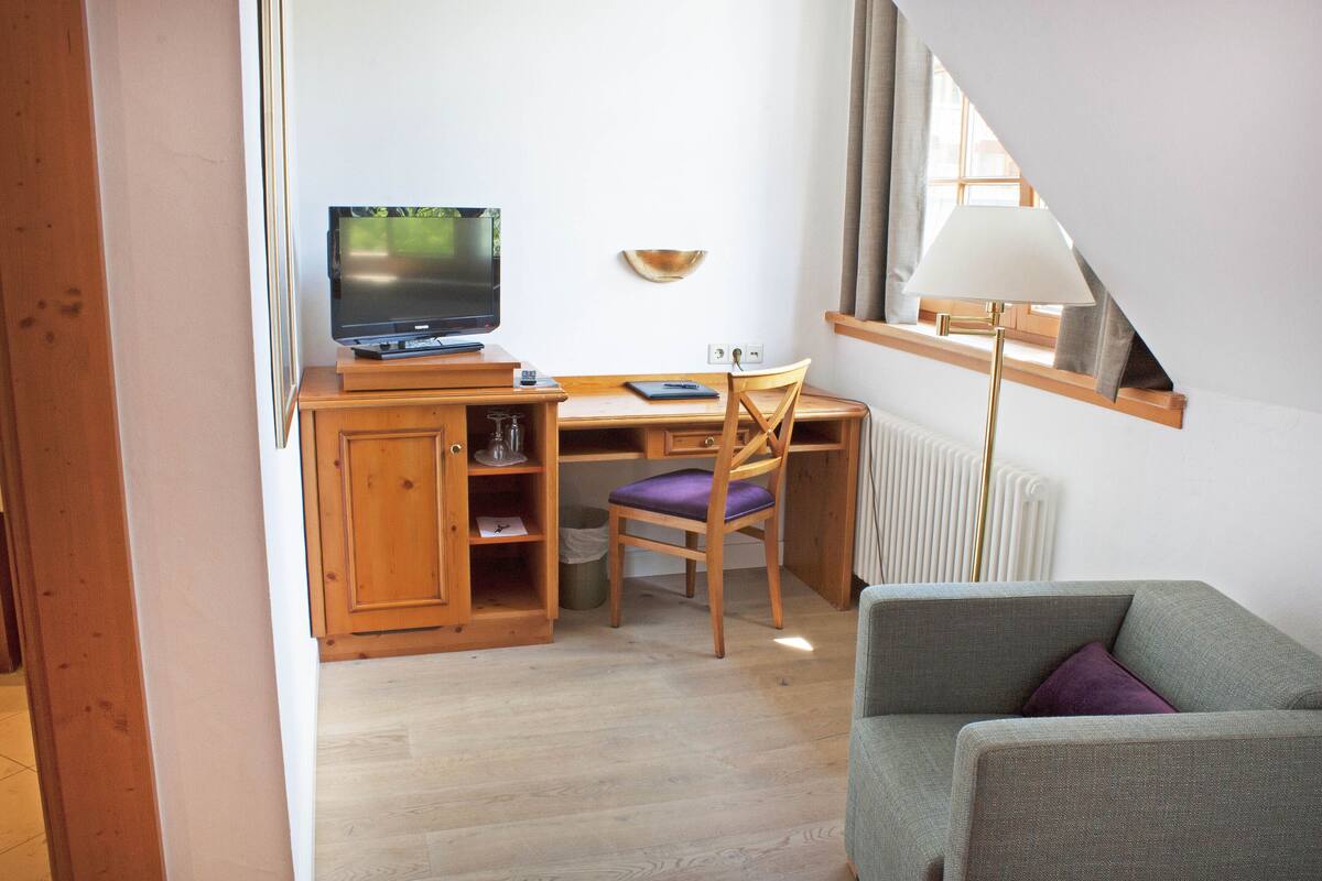 A cozy room with a wooden desk, a television, a chair, a sofa, and a lamp.