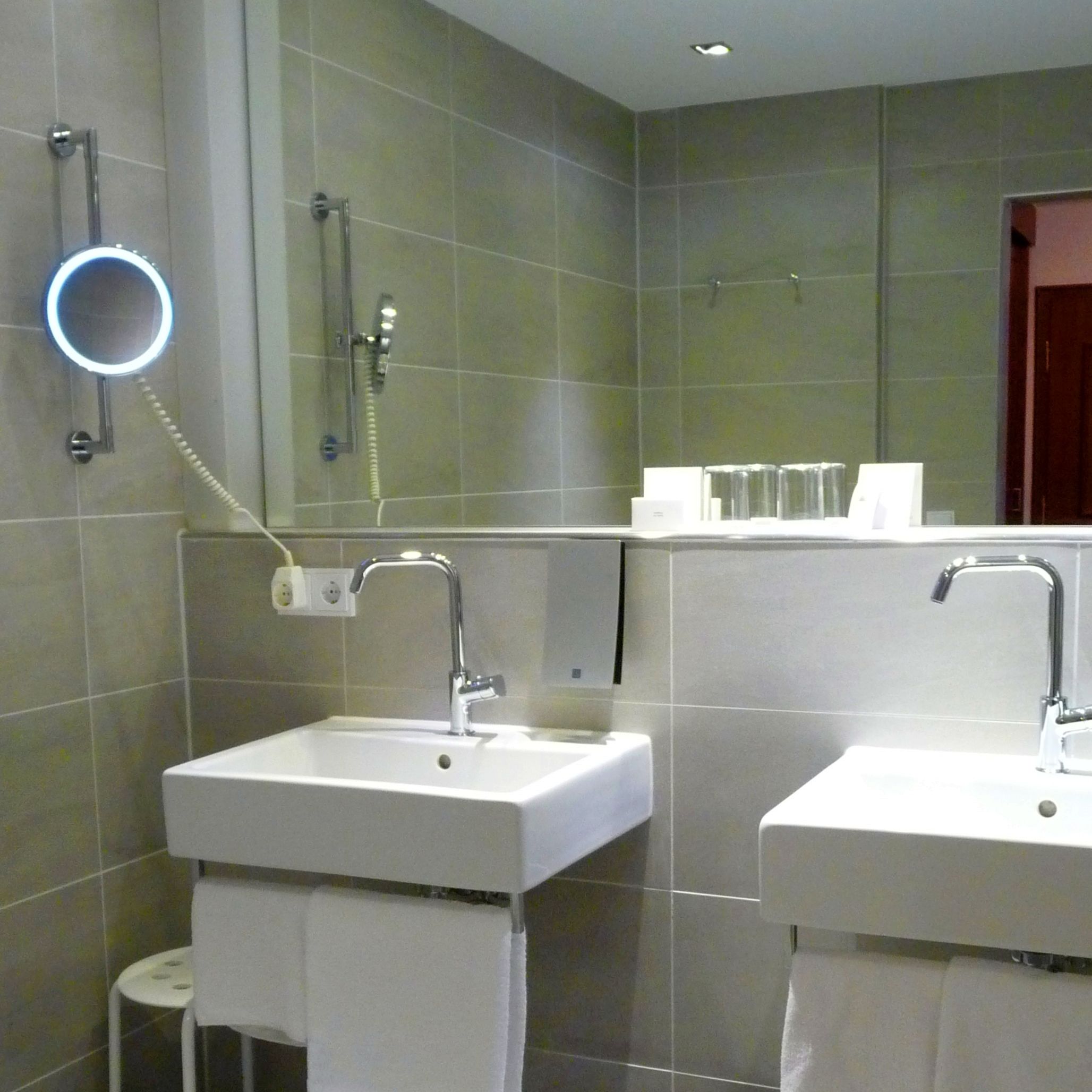 Un baño moderno con dos lavabos, ducha de mano y espejo con luz integrada.