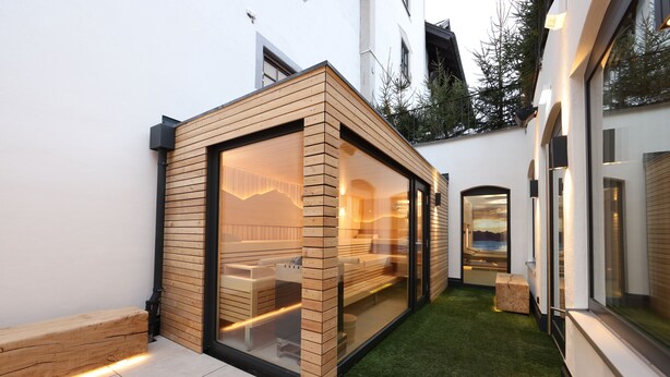 A modern building with a glass enclosure, a wooden bench, and a small grassy area. - Hotel Bayerischer Hof Kur & Sporthotel (Oberstaufen)