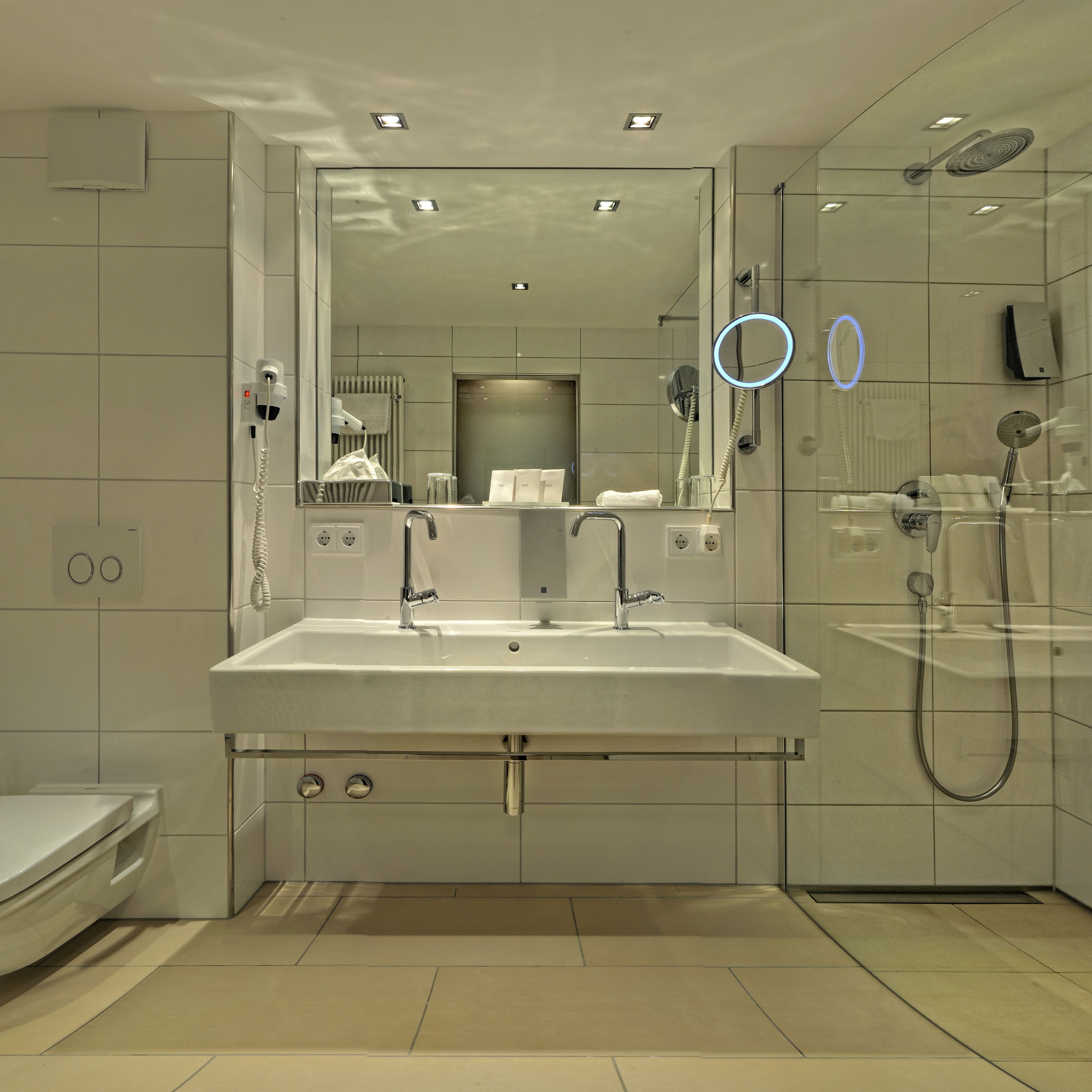 A modern bathroom with a large sink, a glass shower enclosure, and a mirror with a built-in light.