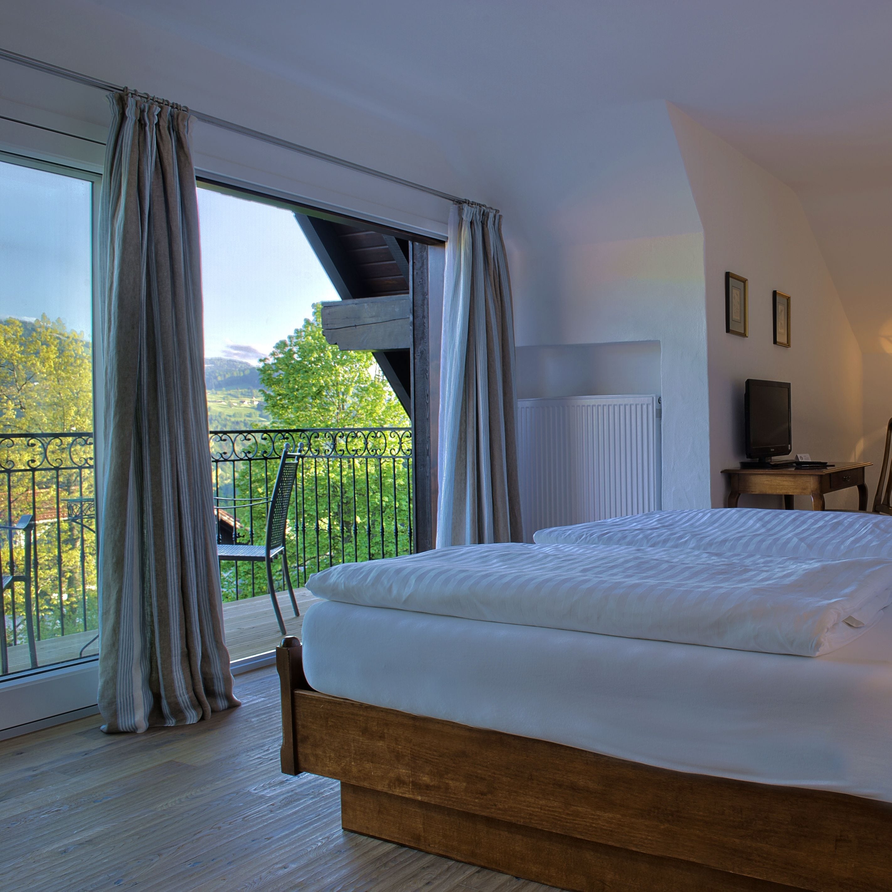 A bedroom with a large bed, a view of a balcony with a chair, and a radiator on the wall.