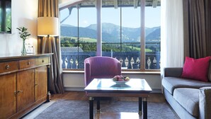 A room with a view of mountains, a sofa, a table with a bowl of fruit, and a cabinet. - Hotel Bayerischer Hof Kur & Sporthotel (Oberstaufen)