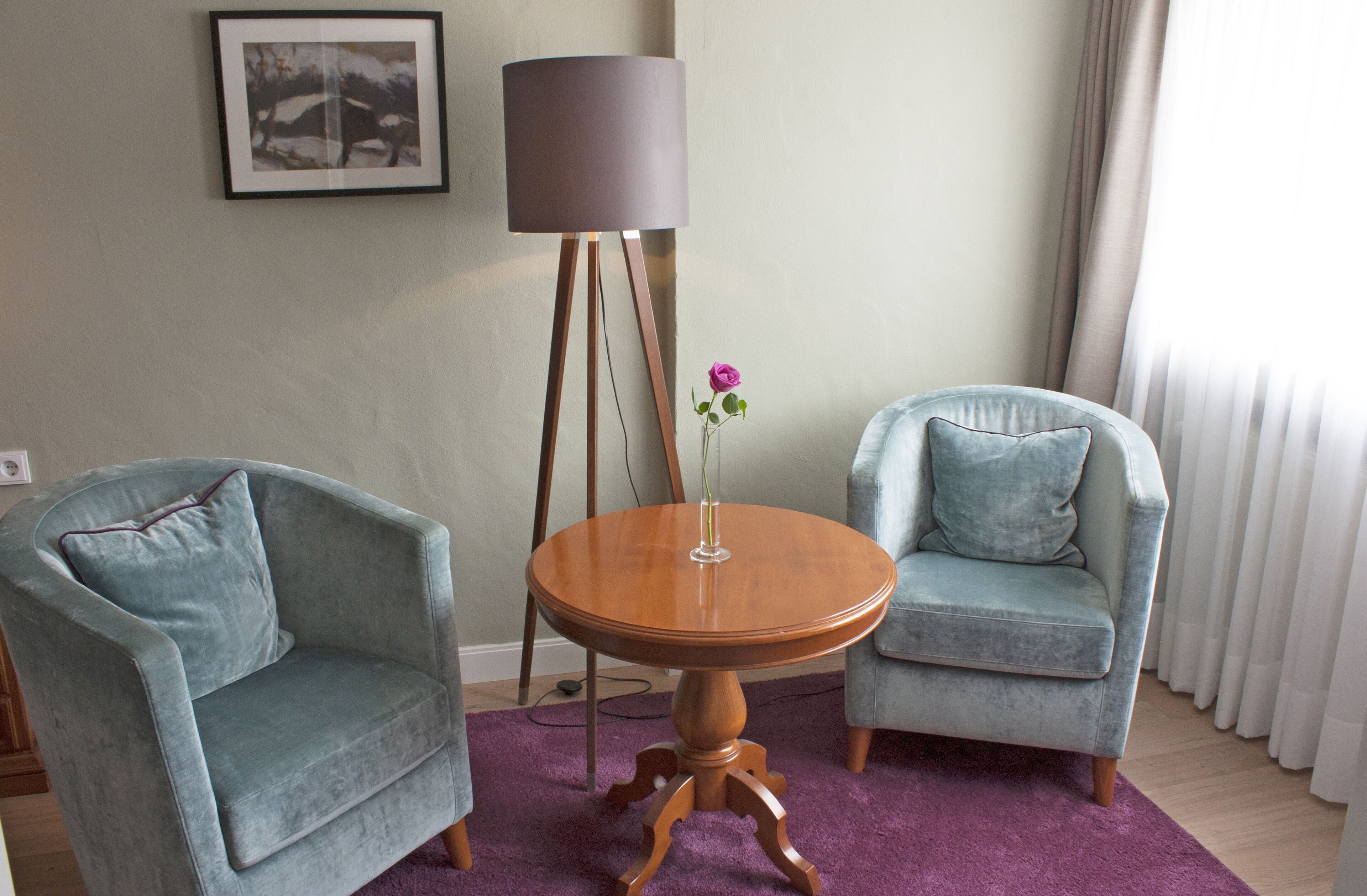 A room with two armchairs, a round wooden table, a floor lamp, and a framed picture on the wall.