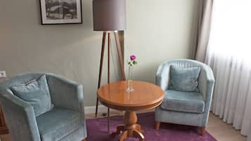 A room with two armchairs, a round wooden table, a floor lamp, and a framed picture on the wall.