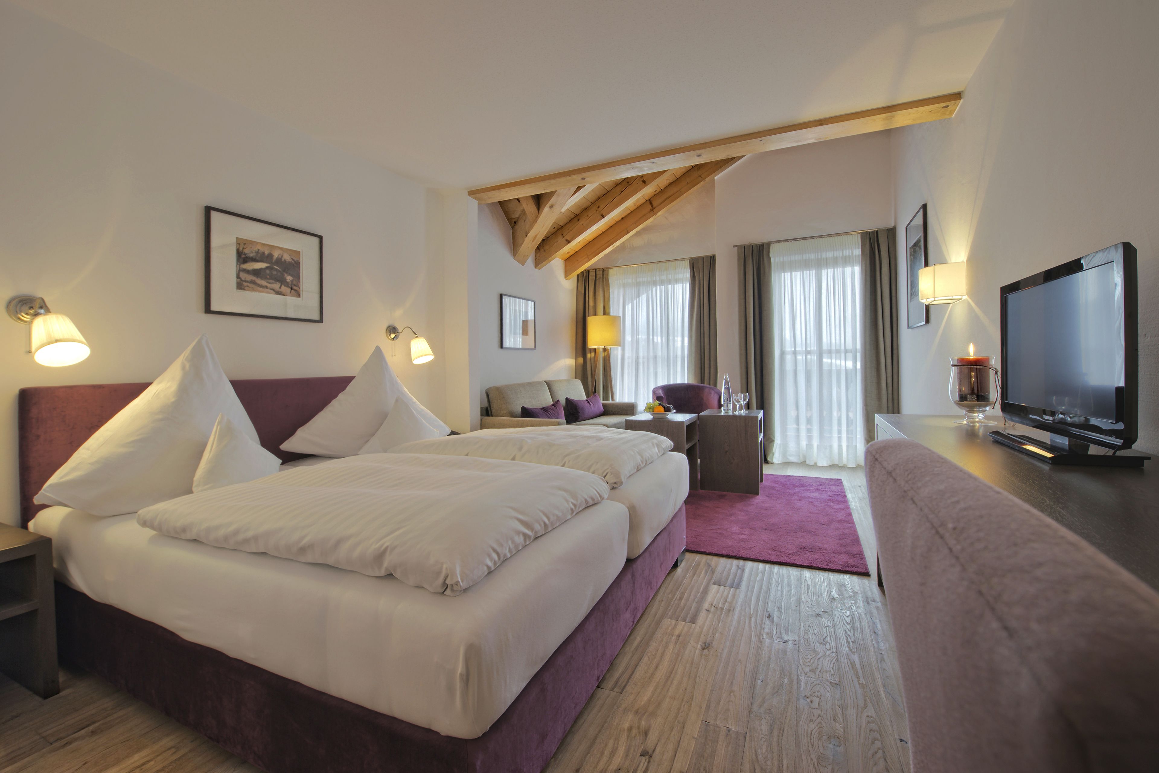 Habitació d'hotel amb dos llits, televisió, escriptori i finestra amb cortines.