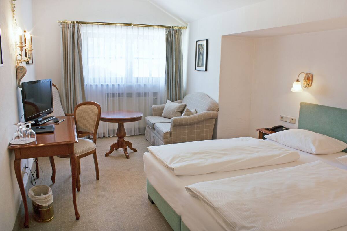 A hotel room with a bed, a desk with a computer, a chair, a small table, and a television.