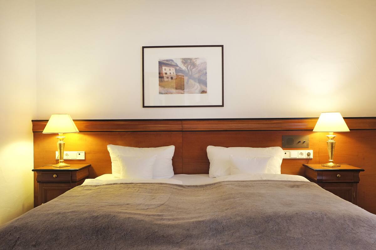 A neatly made bed with a gray blanket, two bedside lamps, and a framed picture on the wall.