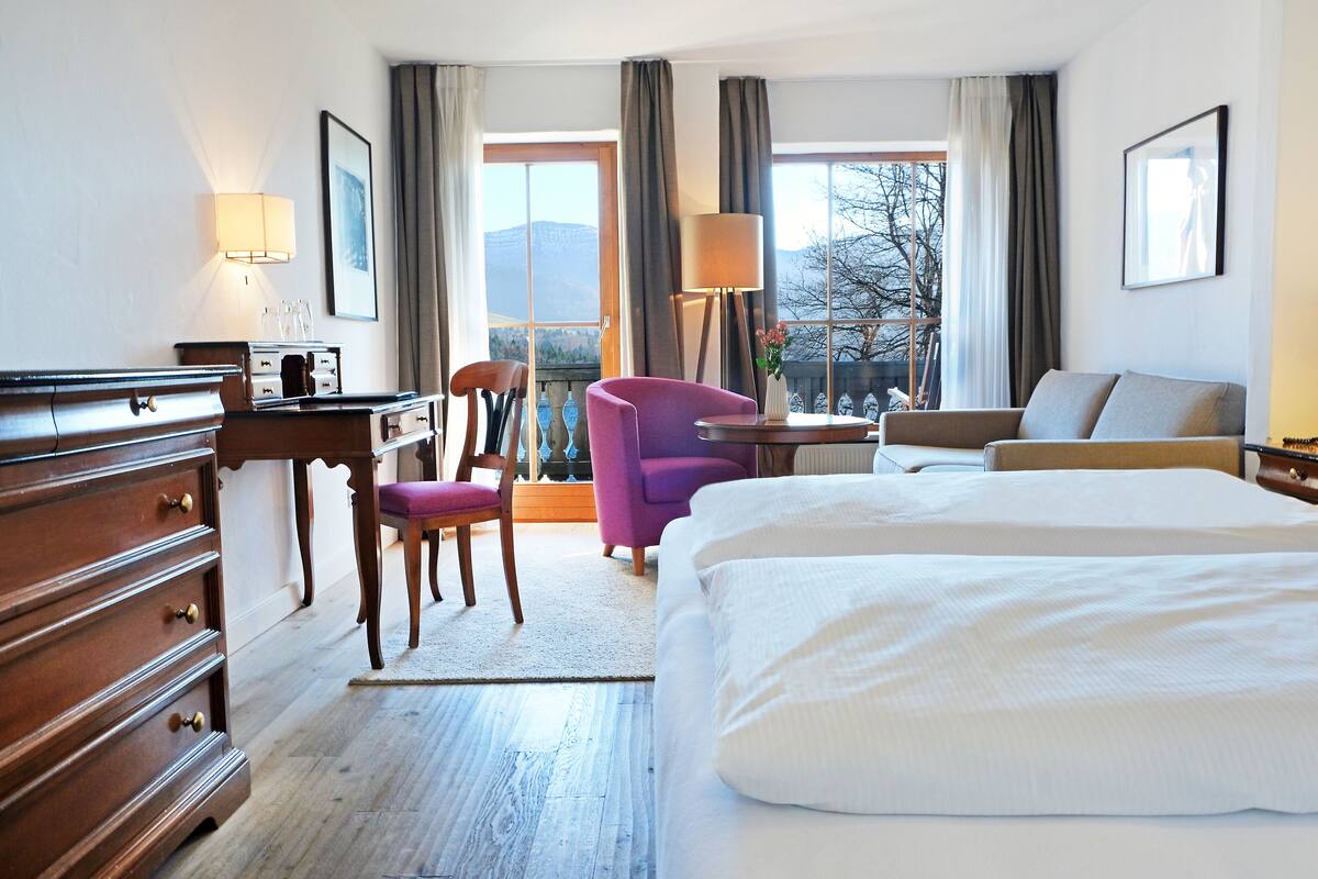 A hotel room with a large bed, a desk with a lamp, a chair, and a view of the outdoors.