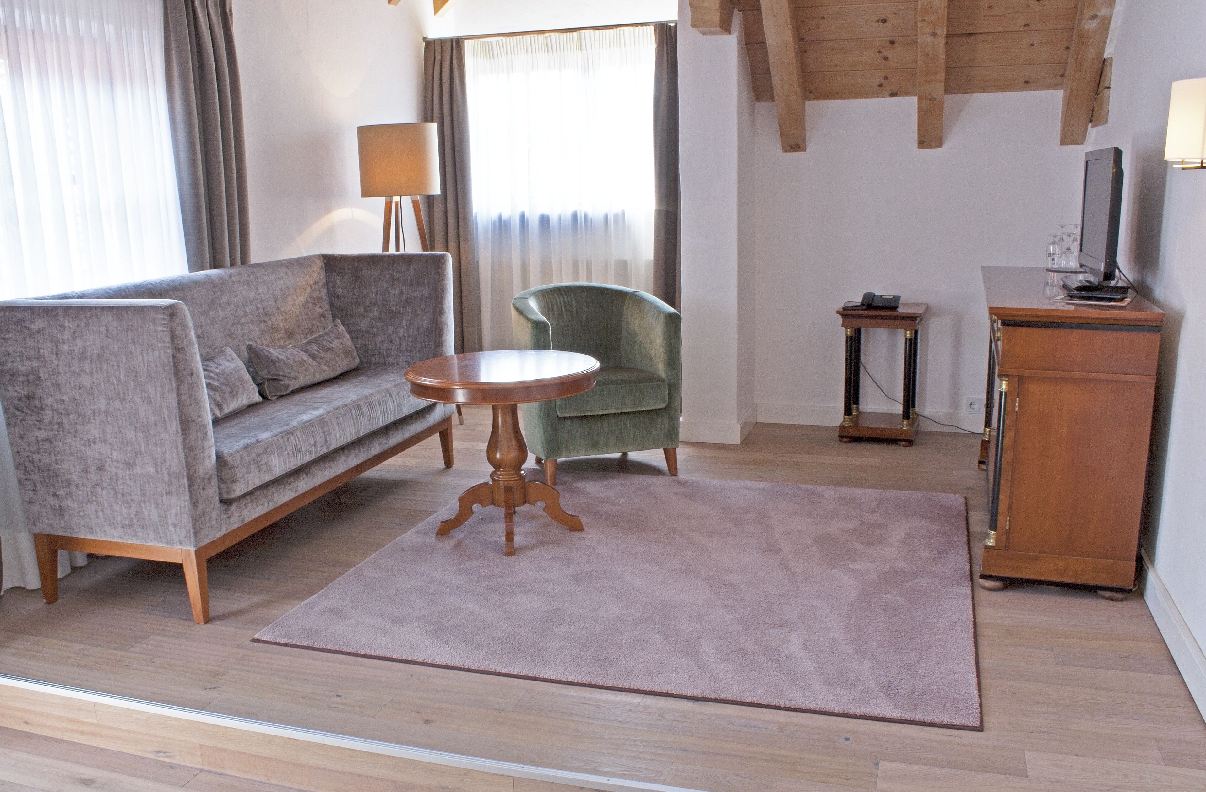 A living room with a sofa, armchair, round table, and a wooden cabinet.