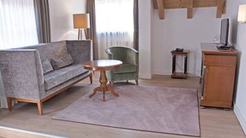 A living room with a sofa, armchair, round table, and a wooden cabinet.