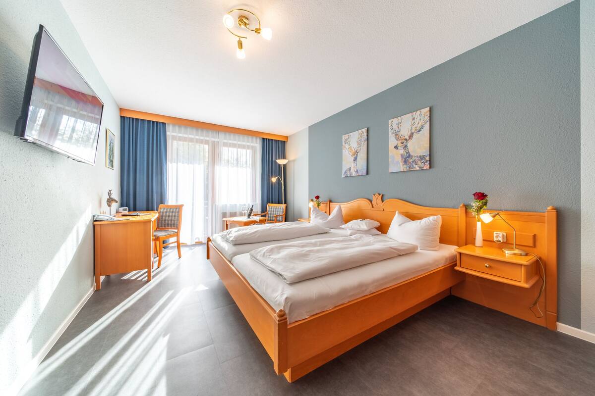 A hotel room with a large bed, a desk, a chair, and a TV mounted on the wall.