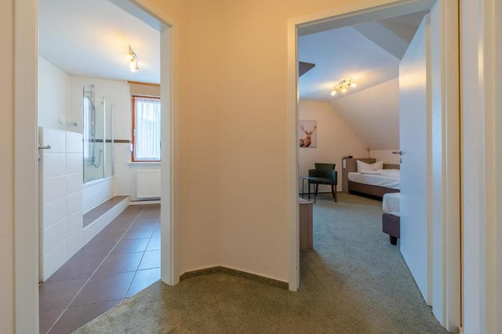 A hallway leading to a bedroom with a bed, a chair, and a small table.