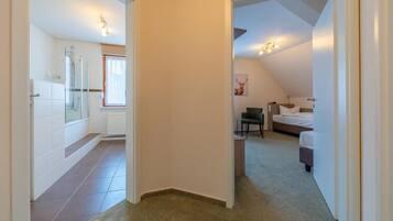 A hallway leading to a bedroom with a bed, a chair, and a small table.