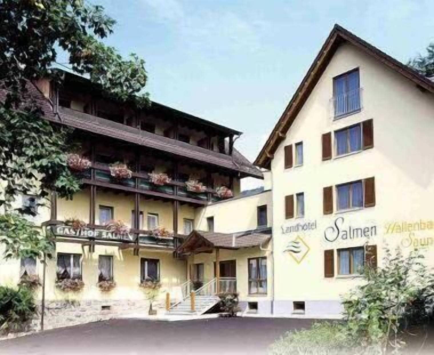 A hotel with a traditional Alpine architectural style, featuring a balcony with hanging flower baskets, a staircase leading to the entrance, and a sign indicating it is a 'Gasthof'.