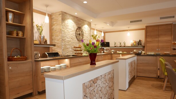 A modern kitchen with wooden cabinets, a central island, and a stone accent wall. - Landhotel Salmen (Oberkirch)