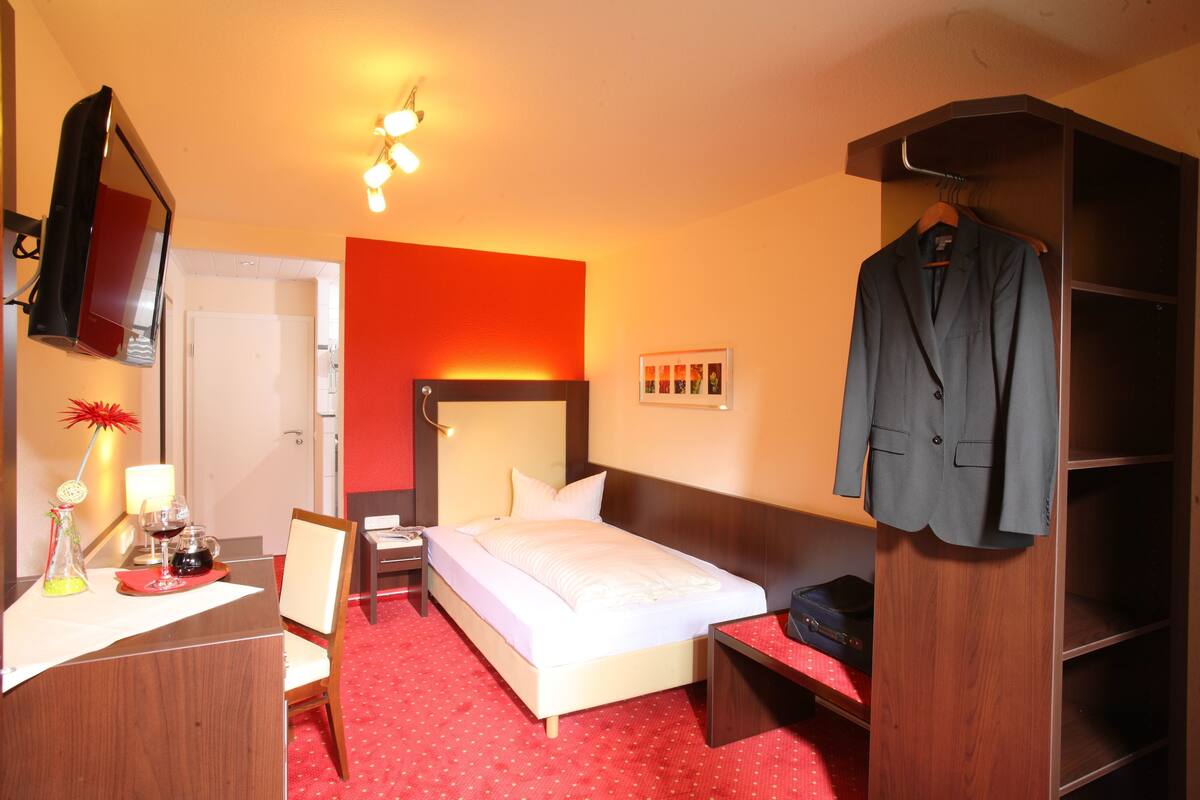 A hotel room with a bed, bedside table, chair, wardrobe, and a mirror.