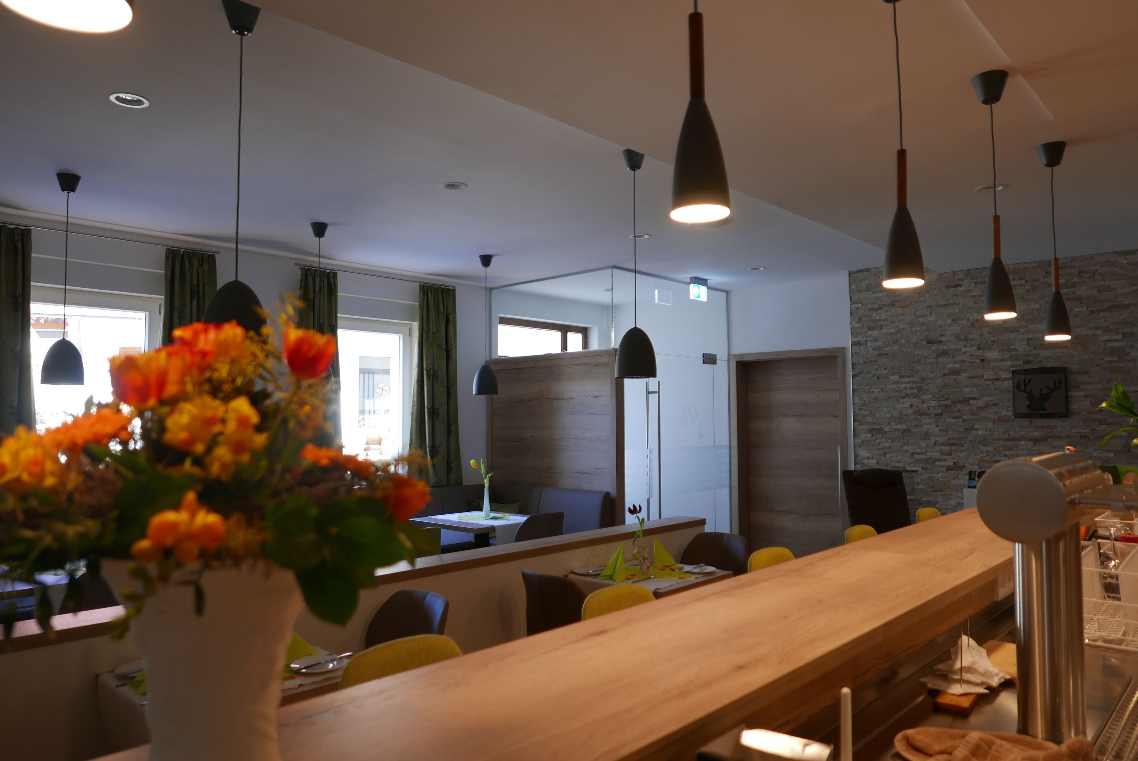 Een moderne eetruimte met een lange houten tafel, zwarte hanglampen en een bloemenvaas.