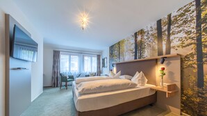 A hotel room with a large bed, a desk, a chair, a TV, and a wall with a nature-themed mural. - Landhotel Salmen (Oberkirch)