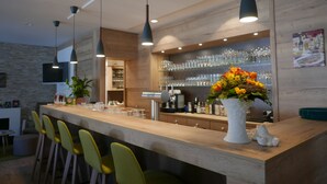 A modern bar area with a wooden counter, green chairs, and a white vase with flowers. - Landhotel Salmen (Oberkirch)