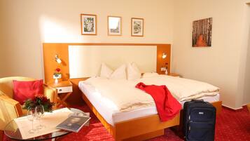 Ein Hotelzimmer mit Bett, Nachttischen, einem Sessel, einem Glastisch mit roter Tischdecke und einem Koffer.