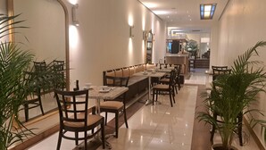 A restaurant with a long counter, cushioned booths, and chairs. There are potted plants and a large mirror on the wall. - Hôtel de la Poste (Esch-sur-Alzette)