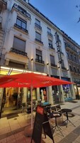 Un edificio de varios pisos, con mesas al aire libre y sombrillas rojas, y un letrero de Coca-Cola.
