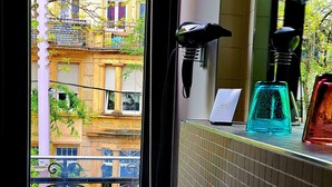 A bathroom with a sink, a window with a view of buildings, and a mirror with a light fixture. - Hôtel de la Poste (Esch-sur-Alzette)