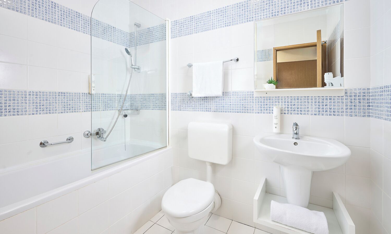 Ein modernes Badezimmer mit einer gläsernen Dusche, einer weißen Toilette, einem Standwaschbecken und einem Spiegel über dem Waschbecken.