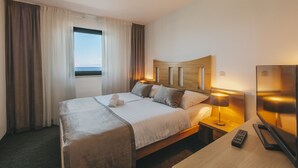 A hotel room with a large bed, a TV, a bedside table, and a window with curtains. - Veya Maradiso Hotel by Aminess  (Omisalj)