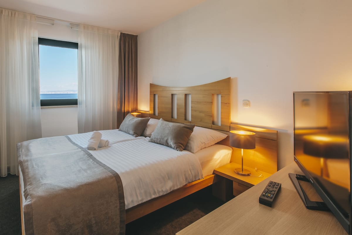 Quarto de hotel com uma cama grande, televisão, mesa de cabeceira e janela com cortinas.