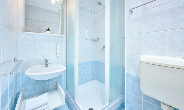 A bathroom with a sink, toilet, shower, and a glass-enclosed shower stall.