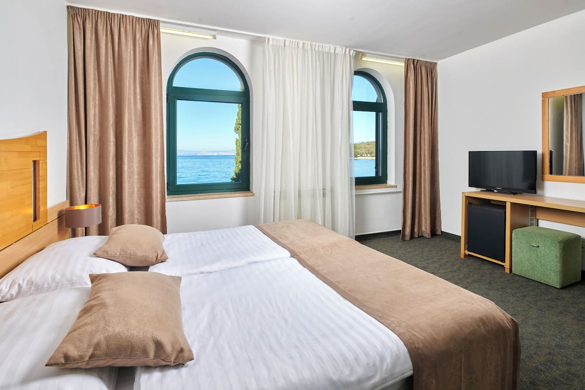 Quarto de hotel com cama, secretária com televisão e amplas janelas com cortinas.