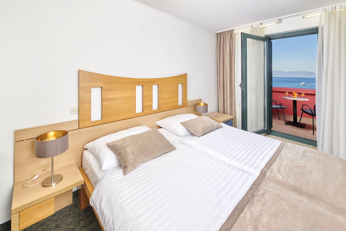 Quarto de hotel com cama, mesas de cabeceira e vista para o mar.