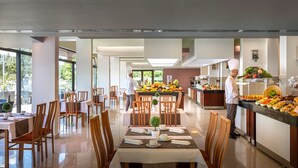 A modern dining area with wooden chairs and tables, a buffet counter with various food items, and a chef preparing food. - Veya Maradiso Hotel by Aminess  (Omisalj)