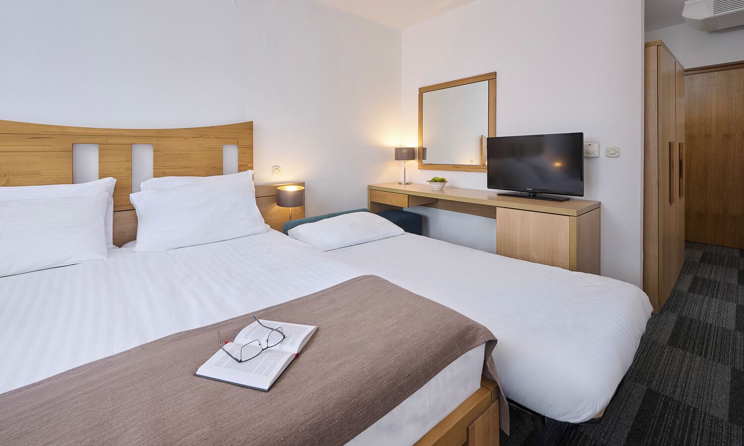 A hotel room with two beds, a TV, a mirror, and a desk with a lamp.