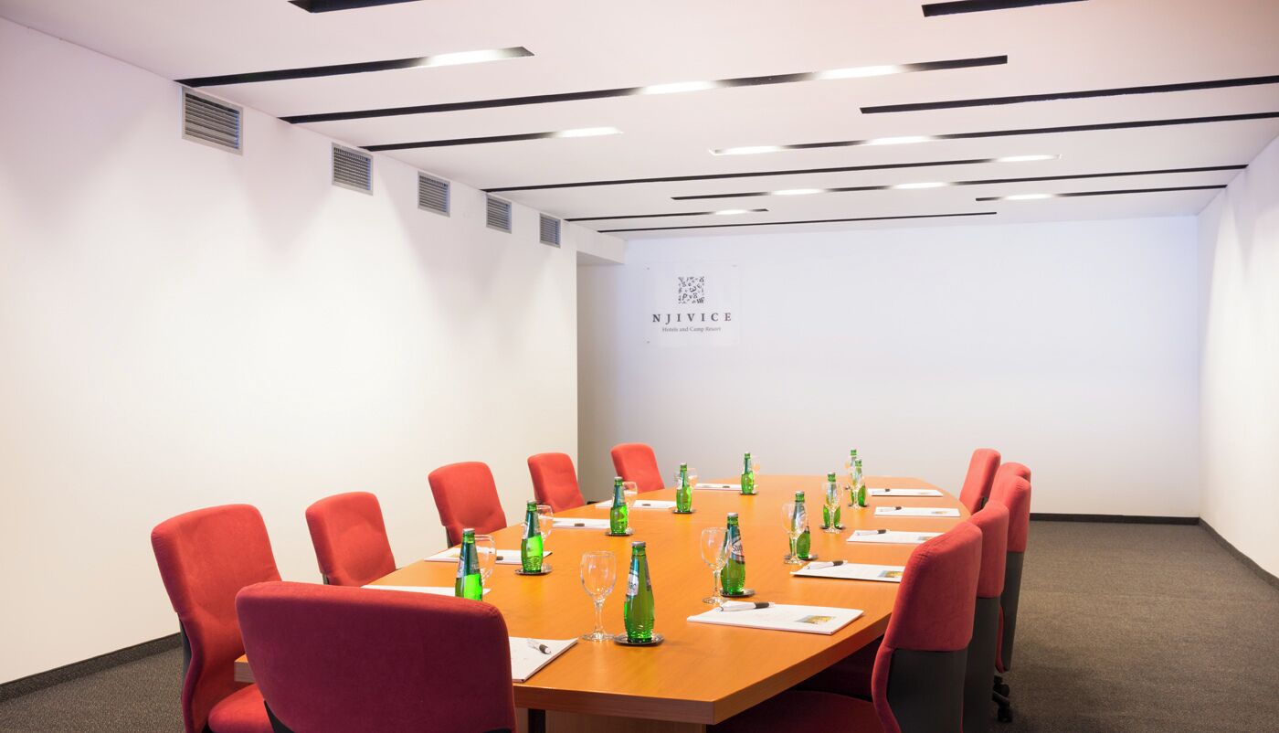 A conference room with a long table, red chairs, and green bottles on the table.