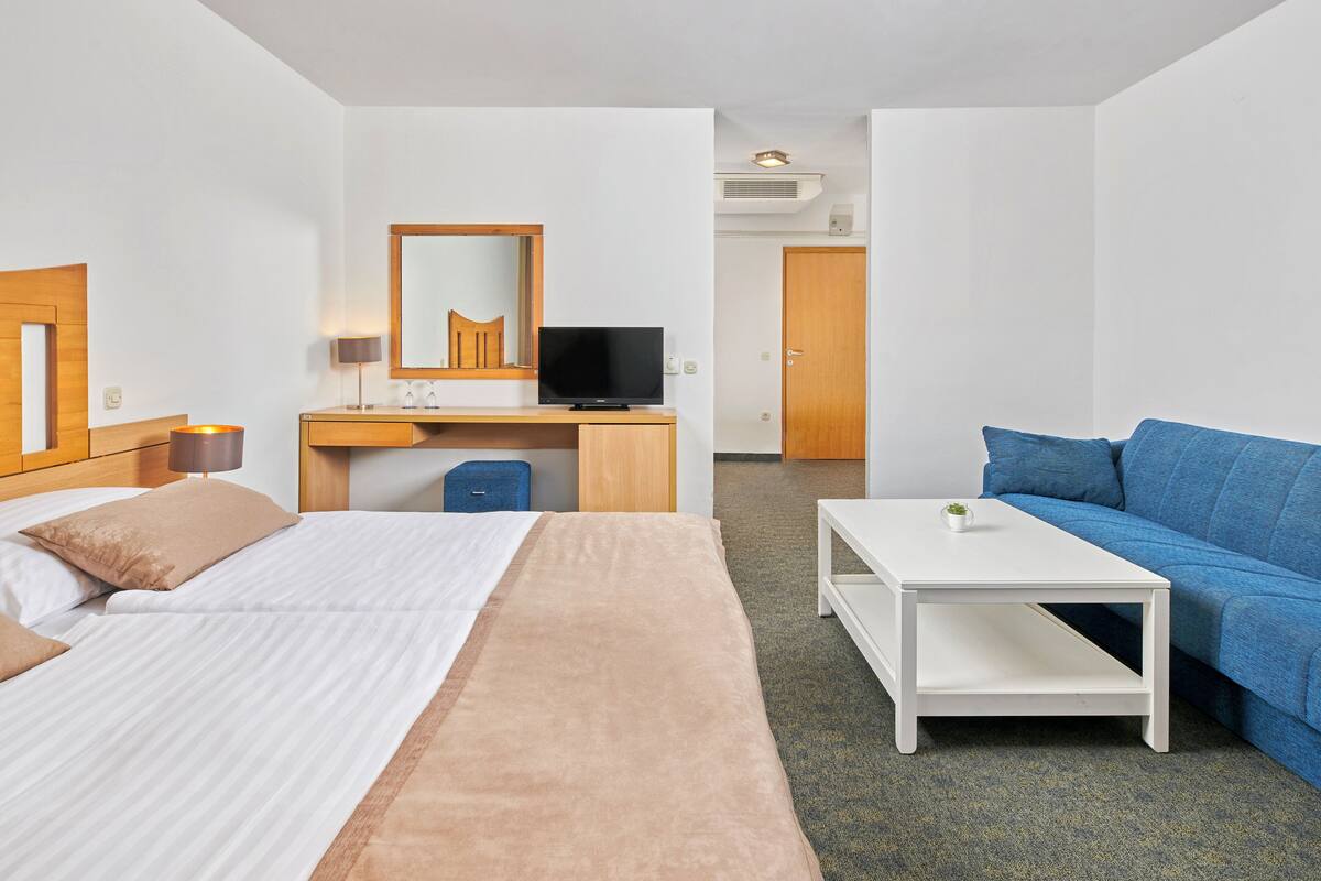 Quarto de hotel com cama, escrivaninha com computador, sofá e uma pequena mesa.
