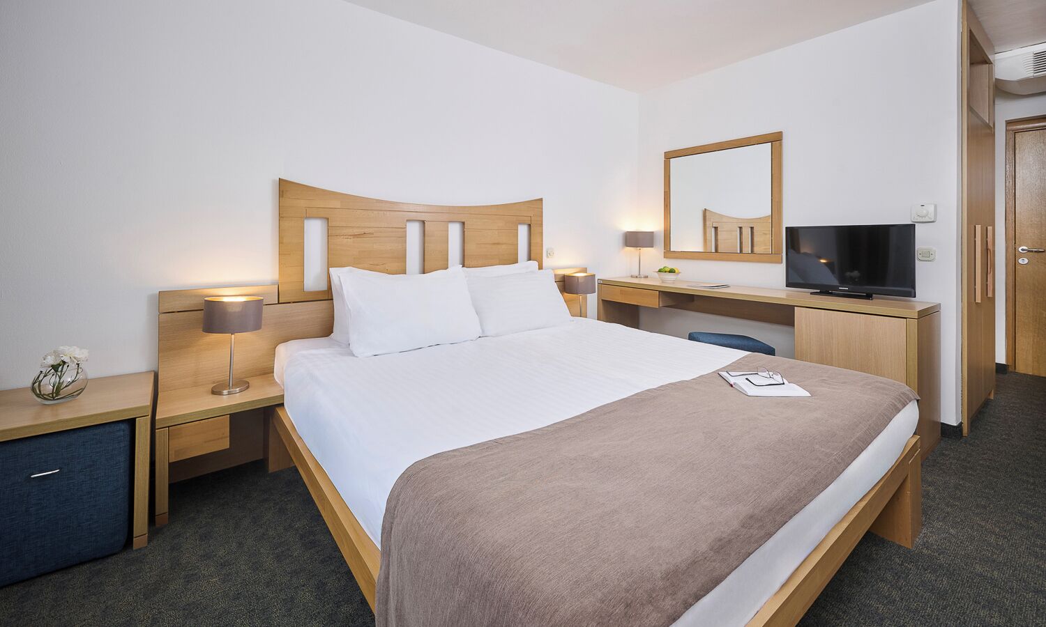 Habitación de hotel con cama, mesitas de noche, escritorio, televisor y espejo.