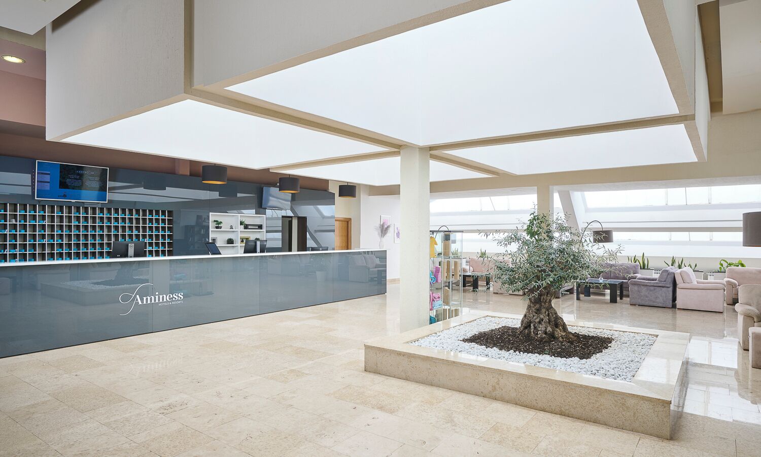A hotel lobby with a reception desk, seating area, and a central plant.