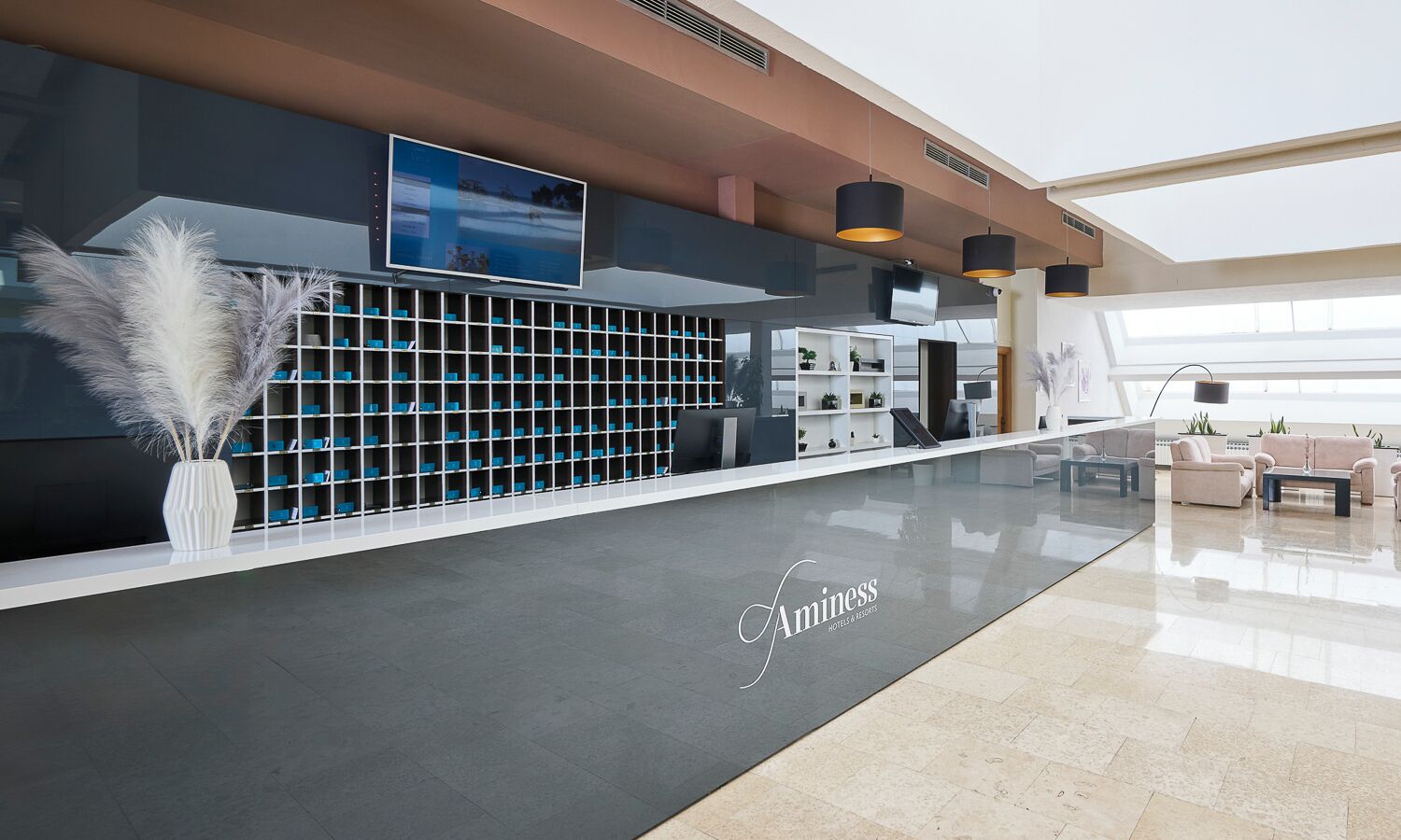 A hotel reception area with a modern design, including a reception desk, seating area, and a large screen.
