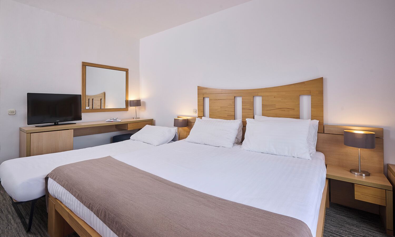 Una habitación de hotel con una cama grande, mesitas de noche, un televisor y un espejo.