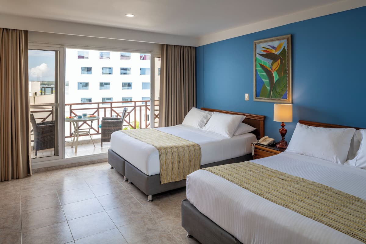 A hotel room with two beds, a balcony with a table and chairs, and a view of a building.