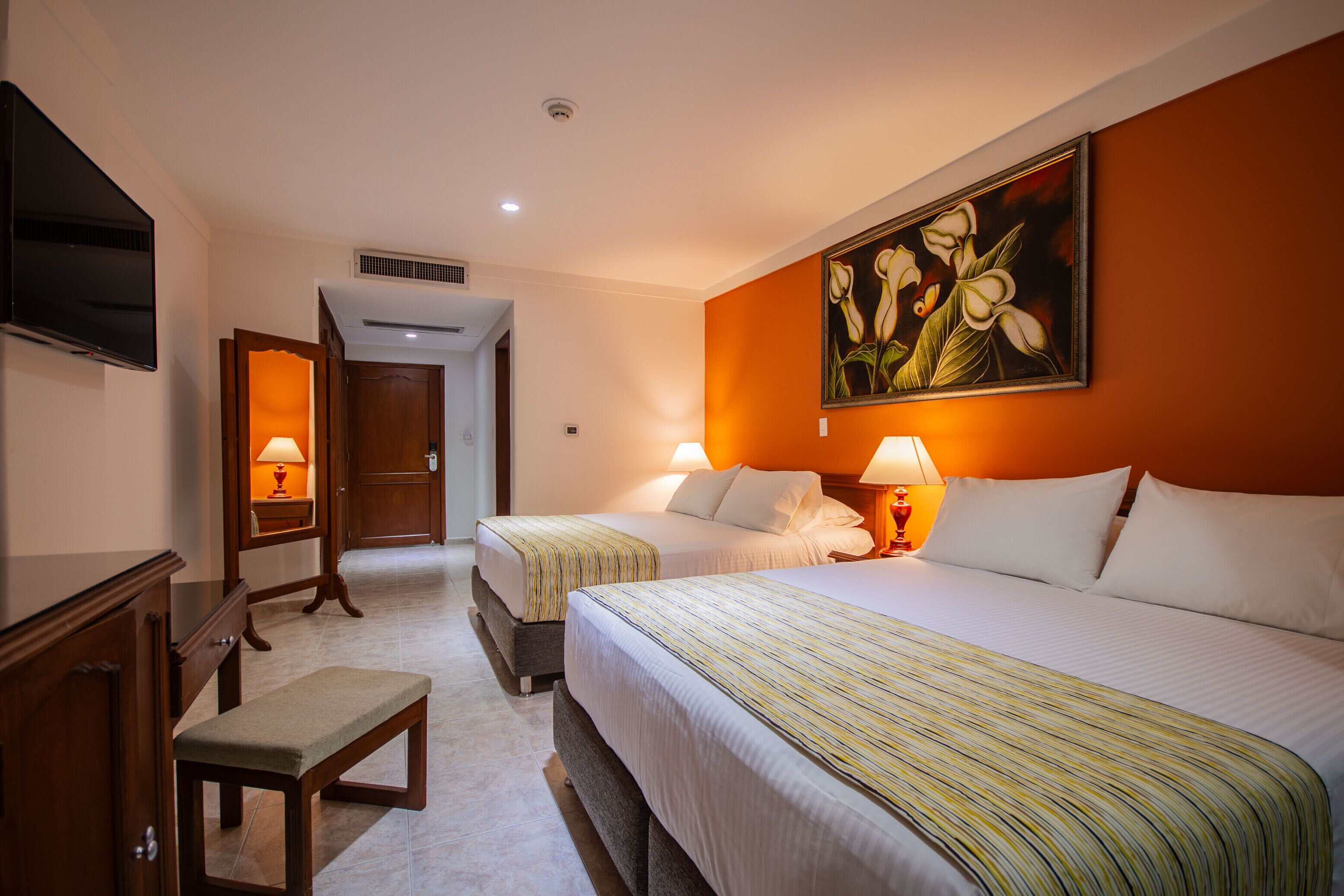 Habitación de hotel con dos camas, un televisor, un banco y un cuadro en la pared.