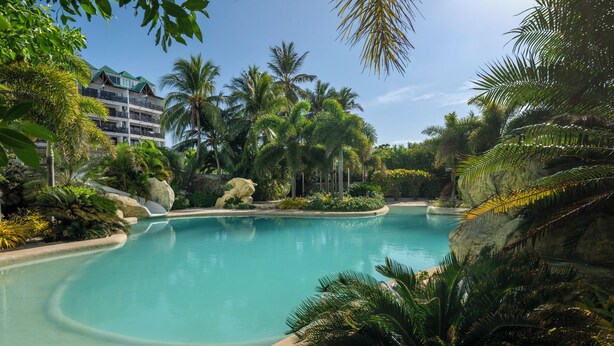 A resort pool surrounded by lush tropical vegetation and a multi-story building with balconies. - Hotel Arena Blanca (San Andrés)
